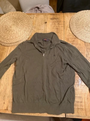 Olivgrön morris halv zip - Snygg olivgrön morris zip m och hög krage. Tröjan har långa ärmar, ribbade muddar och en diskret broderad logga på bröstet. Perfekt för lager-på-lager och passar till många olika stilar.ny pris runt 1200kr