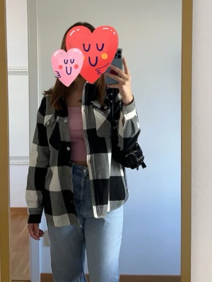 Svartvit rutig overshirt - Säljer en oversized svartvit rutig overshirt med stora rutor och knappar framtill. Skjortan har två bröstfickor med lock och knapp samt klassisk krage. Perfekt att slänga över en t-shirt eller hoodie för en chill look.