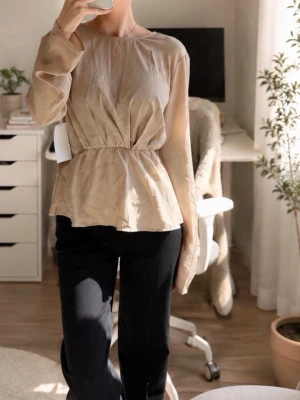 NA-KD champagnefärgad blus med V-ringad rygg – stl 34 - Helt ny champagnefärgad blus från NA-KD! Endast provad och säljs med prislapp kvar.  Elegant modell med vacker V-ringad omlott rygg, långärmade ärmar och smickrande resår i midjan som ger en fin, feminin silhuett. Den lätt draperade modellen faller fint över kroppen.  - Champagne/beige - Storlek EU 34 - Ny med prislapp - Nypris 499 kr  Perfekt till exempelvis kostymbyxor, jeans eller kjol.