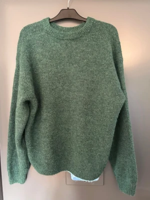 Grön stickad tröja  - Mysig grön stickad tröja. Tröjan har en oversized passform och ribbstickade muddar vid ärmslut och nederkant. Perfekt för höst och vinter och enkel att matcha med jeans eller kjol. Köpt på weekday, aldrig använd och med prislapp kvar! Nypris: 600kr
