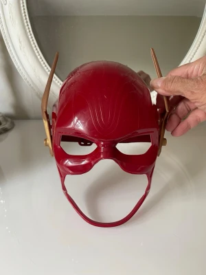 Röd Flash mask cosplay - Röd The Flash-mask för maskerad, unisexmodell med guldfärgade blixtdetaljer på sidorna. Justerbart band bak så den går att spänna runt huvudet.