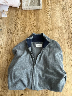 Grå ziptröja från Pier One - Mjuk grå ziptröja från Pier One med hög krage och ribbade muddar. Tröjan har två fickor framtill och dragkedja hela vägen. Perfekt för lager på lager och enkel att matcha med olika outfits.