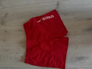 Röda badbyxor från Speedo - Snygga röda badbyxor från Speedo med vitt logotryck på ena benet. Klassisk modell med resår i midjan och ficka bak. Perfekta för stranden eller poolen. Tillverkade i snabbtorkande material. Storlek okänd men skulle tippa på S alternativt M men små i storleken 