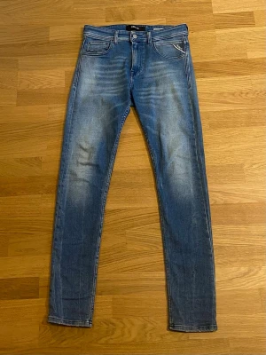 Blå slim fit jeans från Replay - Säljer ett par blå slim fit jeans från Replay med snygga slitningar och tvättade detaljer. Klassisk femficksmodell med dragkedja och knapp. Perfekta för dig som gillar en smalare passform och vill ha ett par jeans som sticker ut lite extra. Nypris 1200kr. Hör av dig vid eventuella funderingar. Mvh. 
