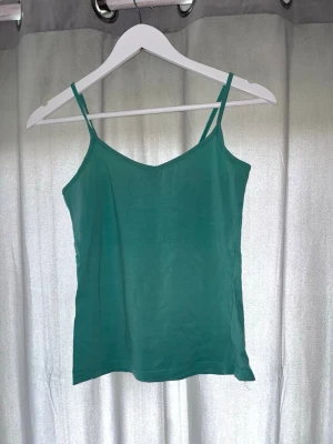 Grön linnetopp från H&M - Snygg grön linnetopp från H&M med smala axelband och v-ringad hals. Perfekt till sommaren och enkel att matcha med olika stilar. Tillverkad i mjuk bomull för en bekväm känsla.