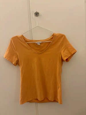 Orange v-ringad t-shirt - Snygg orange t-shirt med v-ringning och korta ärmar. Enkel och stilren design som passar perfekt till jeans eller kjol. Tillverkad i mjukt bomullsmaterial för en bekväm känsla hela dagen.