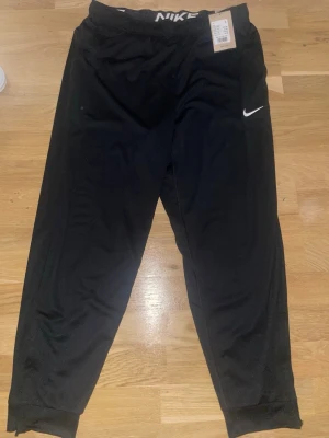  Nike Totality Byxor  - Snygga svarta träningsbyxor från Nike med vit logga på benet och resår i midjan. Byxorna har en avslappnad passform och muddar vid bensluten. Perfekta för chill eller träning. Materialet är mjukt och bekvämt.