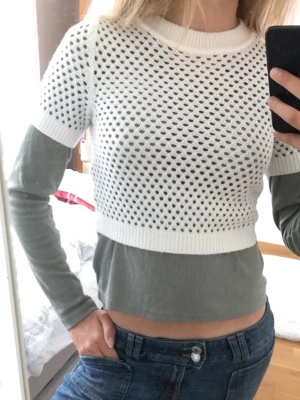 Vit stickad mesh-croppad tröja - Säljer en vit, stickad croppad t-shirt med meshmönster och ribbade kanter.  Enkel att matcha med olika outfits för en trendig look.