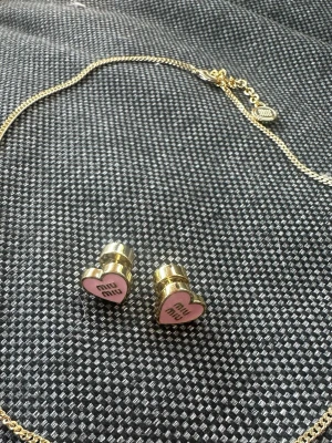 Miu Miu hjärtformade örhängen guldrosa - Säljer ett par supersöta örhängen från Miu Miu i guldtonad metall med hjärtformad front i rosa och logga på framsidan. Perfekt accessoar för dig som gillar statement-smycken med en lekfull touch. Stiftmodell som är enkla att bära.