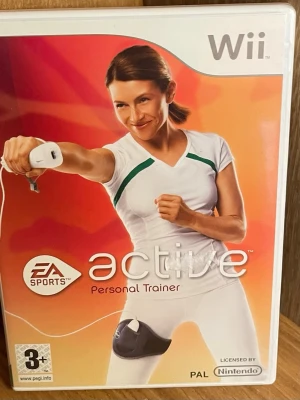 EA Sports Active till Nintendo Wii - Träningsspel till Nintendo Wii där du kan följa ett personligt träningsprogram hemma. Spelet har en vit och orange framsida med en kvinna i träningskläder och kräver Wii-kontroller. Perfekt för dig som vill träna på ett roligt sätt framför TV:n. Perfekt Skick