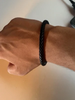 Svart flätat läderarmband - Snyggt svart armband i flätat läder med enkel och stilren design. Armbandet har ett diskret magnetlås i metall som gör det lätt att ta på och av. Perfekt accessoar för en trendig och minimalistisk look.