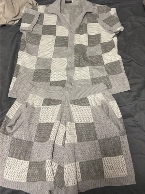 Gråvitrutiga stickade shorts och t shirt - Säljer ett par stickade shorts och t short i grått och vitt med rutigt mönster. Shortsen har bred resår i midjan och fickor på sidorna. Materialet är mjukt och andas, perfekt för en avslappnad look.endast testad 