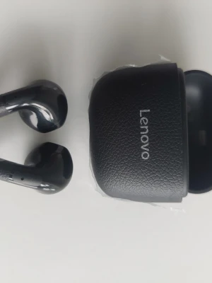 Lenovo svarta trådlösa in-ear hörlurar - Snygga svarta trådlösa in-ear hörlurar från Lenovo med matchande laddningsetui i läderliknande material. Hörlurarna har en stilren, blank finish och ergonomisk form som sitter skönt i öronen. Perfekta för musik, poddar och samtal på språng.