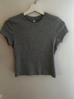 Grå t-shirt från UNIQLO - En enkel och stilren grå t-shirt med rund hals och korta ärmar. Tillverkad i mjuk bomull som känns skön mot huden. Perfekt till jeans eller kjol för en avslappnad look. Aldrig använd❣️