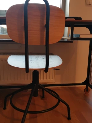 Skrivbordsstol i trä och metall - Säljer en stilren skrivbordsstol med sits och ryggstöd i ljust trä och svart metallram. Stolen har en rund fot och justerbar höjd, perfekt till skrivbordet eller plugghörnan. Enkel, modern design som passar in i de flesta rum.