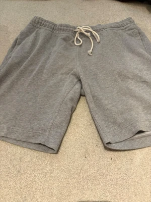 Grå mjukisshorts med snörning - Ett par grå mjukisshorts med elastisk midja och vit snörning framtill. Shortsen har en avslappnad passform och är tillverkade i mjukt bomullsmaterial, perfekta för chill dagar eller träning. HM