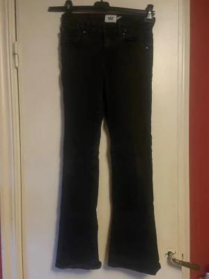 Svarta bootcut jeans(barn)  - Säljer ett par svarta bootcut jeans med klassisk femficksdesign och normal midja. Jeansen har utsvängda ben och är tillverkade i ett stretchigt denimtyg som sitter snyggt. Perfekta för dig som gillar en retroinspirerad look.