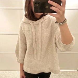 Beige stickad hoodie med trekvartsärm - Mysig beige stickad hoodie med luva och breda snören. Tröjan har korta, vida ärmar och ribbstickade kanter. Perfekt för lager på lager och en avslappnad look. Storlek s💕
