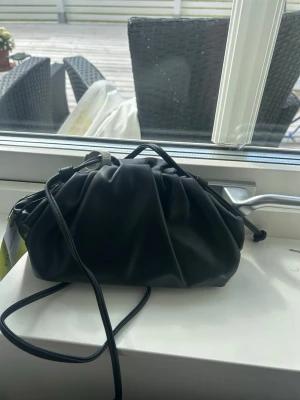 Clutch bag med band - Säljer denna populära svarta clutch bag då jag råkade beställa två stycken. Väskan är helt ny, oanvänd och prislappen är kvar! Axelremmen är lätt att justera för perfekt passform. Väskan är väldigt populär och svår och få tag i!💓 Pris kan diskuteras 