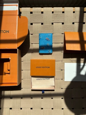 Louis vuitton cardholder blue lagoon - Säljer en blå plånbok från Louis Vuitton med lekfulla motiv av små figurer och båtar. Plånboken är i ett tåligt material, troligen läder, och har en kompakt, rektangulär form. Perfekt för dig som vill ha något unikt och färgglatt i väskan.