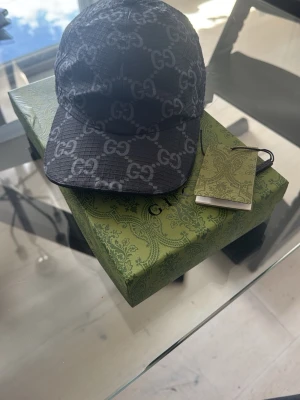 Svart keps från Gucci med GG-mönster - Snygg svart keps från Gucci i storlek M (57 cm) med det klassiska GG-monogrammet över hela kepsen. Tillverkad i ett slitstarkt tyg med justerbar rem bak. Perfekt accessoar för att lyfta din outfit.