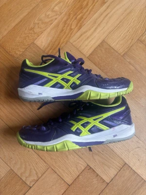 Lila och limegröna Asics sneakers - Säljer ett par snygga sneakers från Asics i lila med limegröna detaljer och vit sula. Skorna har klassisk snörning och slitstark gummisula med bra grepp. Perfekta för dig som gillar sportig stil och vill sticka ut med färg.