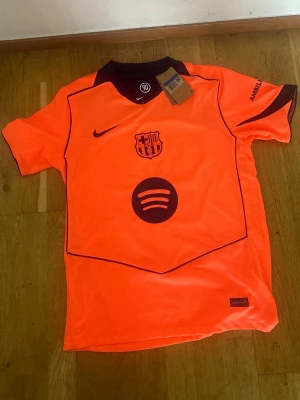 Barcelona matchtröja orange Lamine Yamal - Säljer en Barcelona matchtröja i neonorange med mörklila detaljer. Tröjan har klubbmärke, Nike-logga och Spotify-logga på framsidan samt Lamine Yamal och nummer 10 på ryggen. Korta ärmar, Champions League-märke på ärmen och UNHCR-tryck nedtill bak.