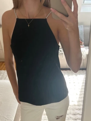 Svart topp - Snygg svart linnetopp med tunna, glittriga axelband och rak halsringning. Toppen är ärmlös och har en enkel, stilren design som passar perfekt till jeans eller kjol. 