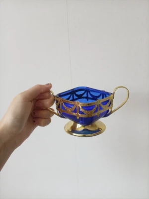 Blå och guldig sockerskål i glas - Unik sockerskål i blått glas med två handtag och detaljer i guld. Skålen har fyrkantig form och står på en liten fot. Perfekt som dekoration eller till servering av sockerbitar. Riktigt snygg vintagekänsla och sticker ut i köket. Den ä avtag bar skålen
