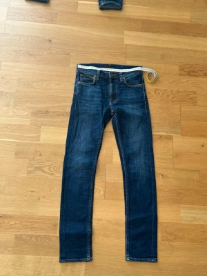 Nästan Helt nya nudie jeans - Jeansen har andvänts under 5 gånger.Snygga mörkblå slim fit jeans med klassisk femficksdesign och kontrastsömmar. Jeansen har en något tvättad look och raka ben. Perfekta för en stilren och avslappnad outfit.