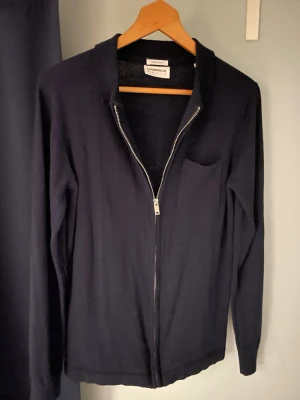 Mörkblå stickad tröja med dragkedja  - Mörkblå stickad cardigan tröja i merinoull. Sitter bra i passformen och är väldigt skön att ha på sig. Den är lätt att matcha till ett par jeans eller chinos vilket blir en enkel men samtidigt väldigt snygg kombination. 