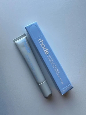 rhode sugarberry Peptide Lip Treatment - Peptide Lip Treatment från rhode i en stilren, ljusgrå tub med blå text och matchande blå förpackning. Läppbalsamet har en modern och minimalistisk design och är perfekt för att återfukta och vårda läpparna. Innehåller 10 ml.
