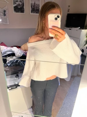 Vit off shoulder stickad tröja - Trendig vit stickad tröja med off shoulder-design och vida ärmar. Tröjan har en lös, croppad passform och är stickad i ett mjukt material som ger en avslappnad look. Perfekt för dig som gillar en stilren och modern vibe.