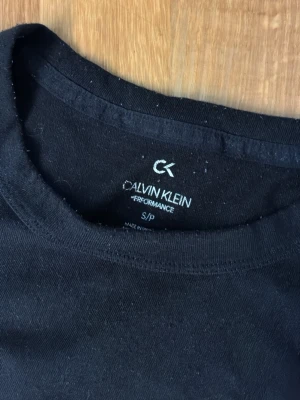 Svart långärmad topp Calvin Klein - Svart långärmad topp från Calvin Klein med stor vit logga framtill. Tillverkad i mjuk bomull, perfekt för en clean och stilren look. Rund halsringning och normal passform.