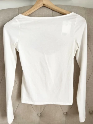 Vit långärmad topp med cut out - Snygg vit långärmad tröja i mjukt och stretchigt material. Figurnära passform och enkel design som känns modern.