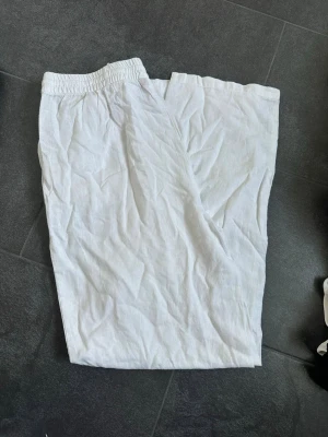Vita linneshorts med resårmidja - Säljer ett par vita shorts i linne med elastisk midja för skön passform. De har en enkel och clean design utan synliga detaljer eller fickor. Perfekta för varma dagar och ger en avslappnad vibe.