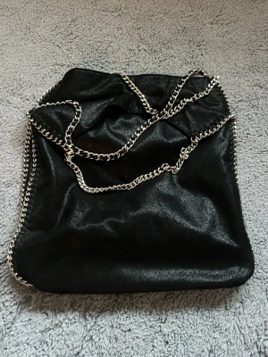 Gina Tricot svart axelväska - Snygg svart axelväska från Gina Tricot. Med silverfärgade kedjedetaljer längs kanterna och som axelrem. One size 