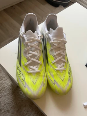 Adidas F50 gulvita fotbollsskor - Säljer ett par Adidas F50 fotbollsskor i en fräsch gul och vit färgkombination med svarta detaljer. Skorna har snörning, och riktigt sköna för bästa känsla på planen. Perfekta för dig som vill sticka ut och få bra grepp. Dem är nästan helt nya använd en träning. Dem är sprejad på affär för att hålla färg bättre även lite vatten skydd. Storlek 39 1/3
