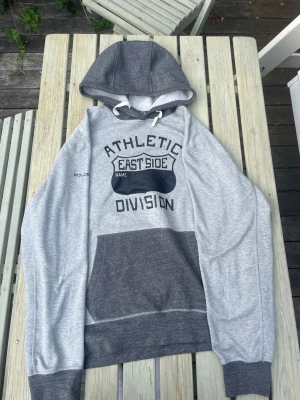 Polo Sport Ralph Lauren Vintage Hoodie | Stl L - Athletic East Side Beskrivning: Snygg grå/mörkgrå huvtröja från Polo Sport Ralph Lauren i storlek L. Coolt "Athletic East Side Division"-tryck på bröstet och Polo-detalj på ärmen. Mjuk och skön kvalitet i gott skick. 