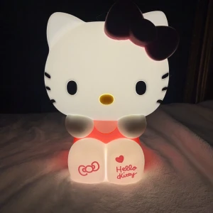 Hello Kitty nattlampa - Hello Kitty nattlampa med en söt design. Den är mjuk, rosa rosett och detaljer. Perfekt för att skapa en mysig atmosfär i sovrummet . Levereras med en fjärrkontroll för enkel användning. 