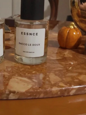 ESSNCE BACCO LE DOUX parfym - Minimalistisk parfymflaska från ESSNCE med doften BACCO LE DOUX. Flaskan är cylindrisk i genomskinligt glas med svart matt kork och vit etikett med svart text. Modern och stilren design som passar perfekt på parfymhyllan. Mer ån halva parfym kvar 