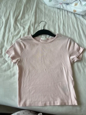 Ljusrosa t-shirt från Gina Tricot - En enkel och stilren ljusrosa t-shirt från Gina Tricot, basically basics-kollektionen. T-shirten har rund halsringning och korta ärmar. Perfekt att matcha med jeans eller kjol för en clean look.