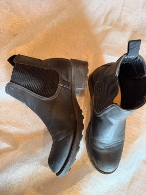 Svarta Chelsea boots med grov sula - Säljer ett par klassiska svarta Chelsea boots i skinnimitation med elastiska paneler på sidorna och grov sula. 
