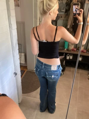 Blå bootcut jeans med fickdetaljer - Säljer ett par blå bootcut jeans med låg midja och snygga fickdetaljer bak. Jeansen har vita sömmar och dekorativa knappar på bakfickorna. Perfekta för dig som gillar en avslappnad och trendig look.dom är helt oanvända köpte för 1299 kr aldrig använda dom är i storlek W27 vilket är S/M