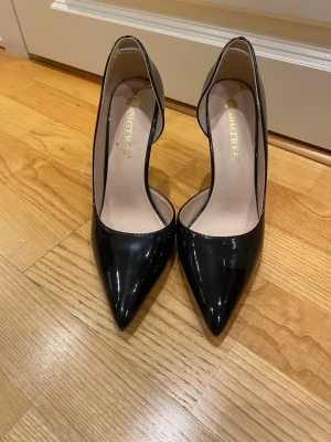 Svarta lackpumps med spetsig tå - Snygga svarta pumps från BIGTREE i glansigt lackmaterial med spetsig tå och hög klack. Klassisk och elegant design som passar till många olika outfits. Klacken är smal och ger en stilren siluett.