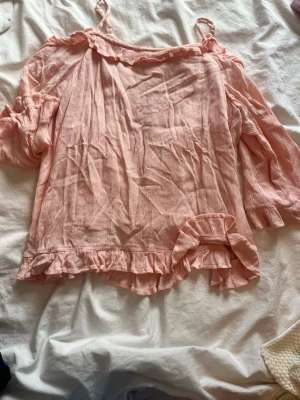 Ljusrosa/ aprikos färgad offshoulder blus med volanger - Supersöt ljusrosa offshoulder blus med tunna axelband och volangdetaljer vid ärmslut och nederkant. Blusen har ett luftigt tyg som ger en avslappnad vibe och långa ärmar med volanger. Perfekt för dig som gillar romantisk stil. Den är i jätte fint skick. 