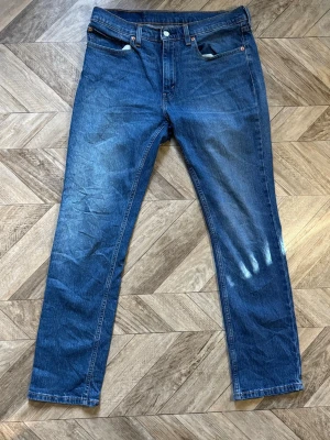 Blåa Levi's 511 - Klassiska blå jeans från Levi's med rak passform och fem fickor. Jeansen har en snygg tvätt med lätt slitning på låret och bakfickor med den ikoniska Levi's-detaljen. Tillverkade i slitstark denim, perfekta för en avslappnad stil. Längd 106cm Bredd 42cm