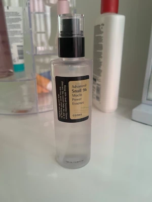 COSRX Advanced Snail 96 Mucin Essence - En genomskinlig plastflaska med svart pump som innehåller COSRX Advanced Snail 96 Mucin Power Essence. Essencen är lättflytande och färglös, perfekt för återfuktning och att stärka hudbarriären. Flaskan rymmer 100 ml och har en stilren, minimalistisk design. Har använt lite men det är endast kanske 5 ml.