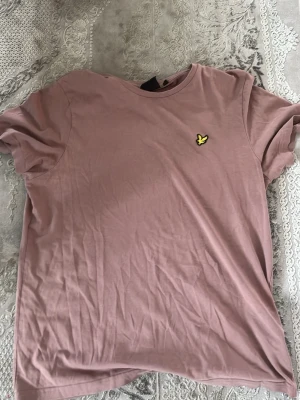 Ljusrosa t-shirt med gul brodyr - Säljer en ljusrosa t-shirt i mjuk bomull med korta ärmar och rund hals. På bröstet sitter en broderad gul fågel som detalj. Enkel och stilren modell som passar till det mesta.
