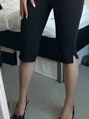 Capribyxor i Small - Säljer ett par svarta Capris med liten slits framtill vid bensluten. De har en medelhög midja och sitter tight mot kroppen. Perfekt för dig som gillar en clean och stilren look. Materialet känns stretchigt och bekvämt.